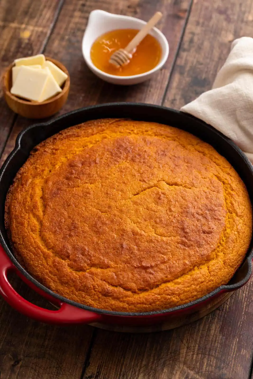 Baked sweet potato cornbread in a cast iron skillet, with bowls of butter and honey in the background.