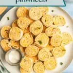 Overhead view of buffalo chicken pinwheels arranged next to a ramekin of ranch dressing on a white platter. Text overlay includes recipe name.