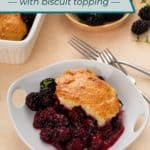 White bowl filled with blackberry cobbler set in front of a bowl of fresh blackberries. Text overlay includes recipe name.