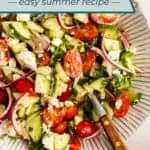Serving spoon in a large bowl of cucumber feta salad. Text overlay includes recipe name.