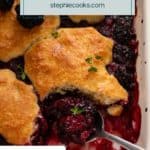Spoon in the corner of a baking dish filled with biscuit-topped blackberry topping. Text overlay includes recipe name.