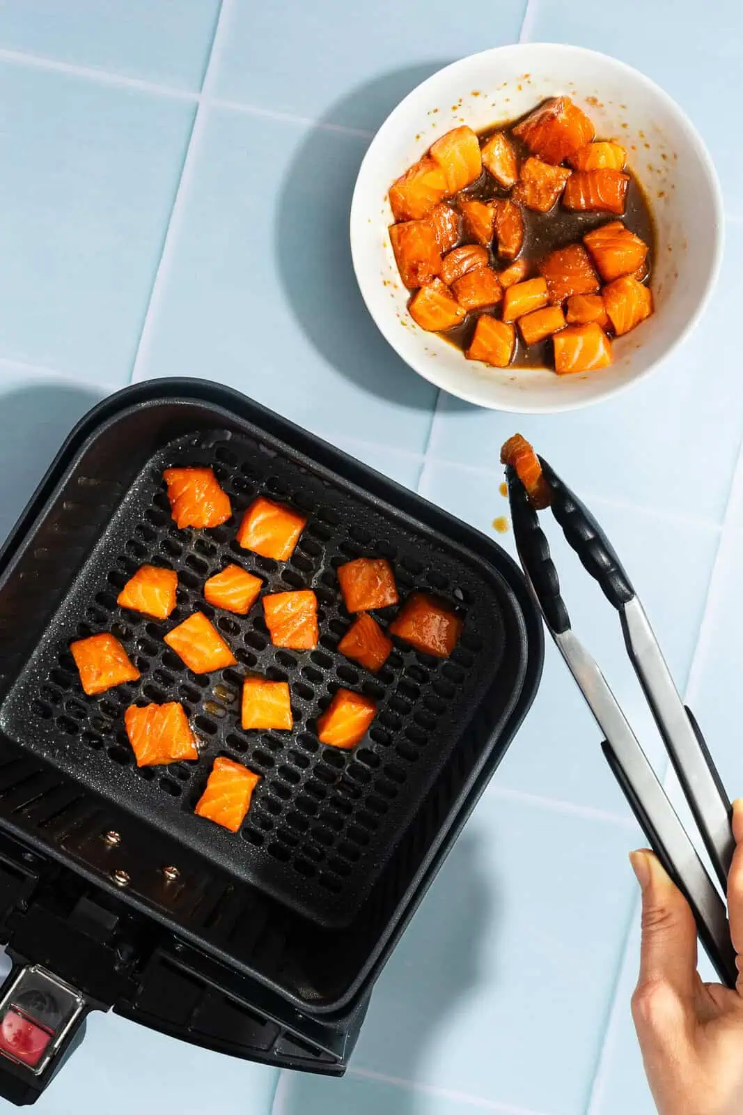 Marinated salmon bites being added to the basket of an air fryer.
