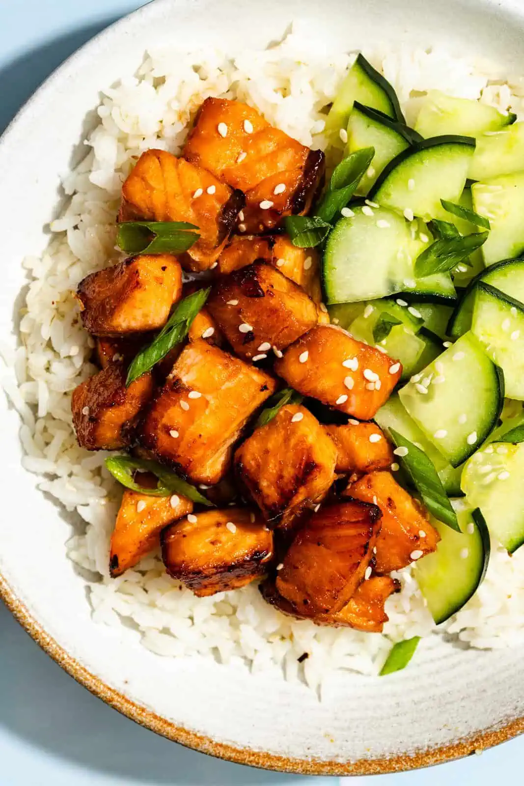 Close up of air fryer salmon bites and sliced cucumbers on a bed of white rice.