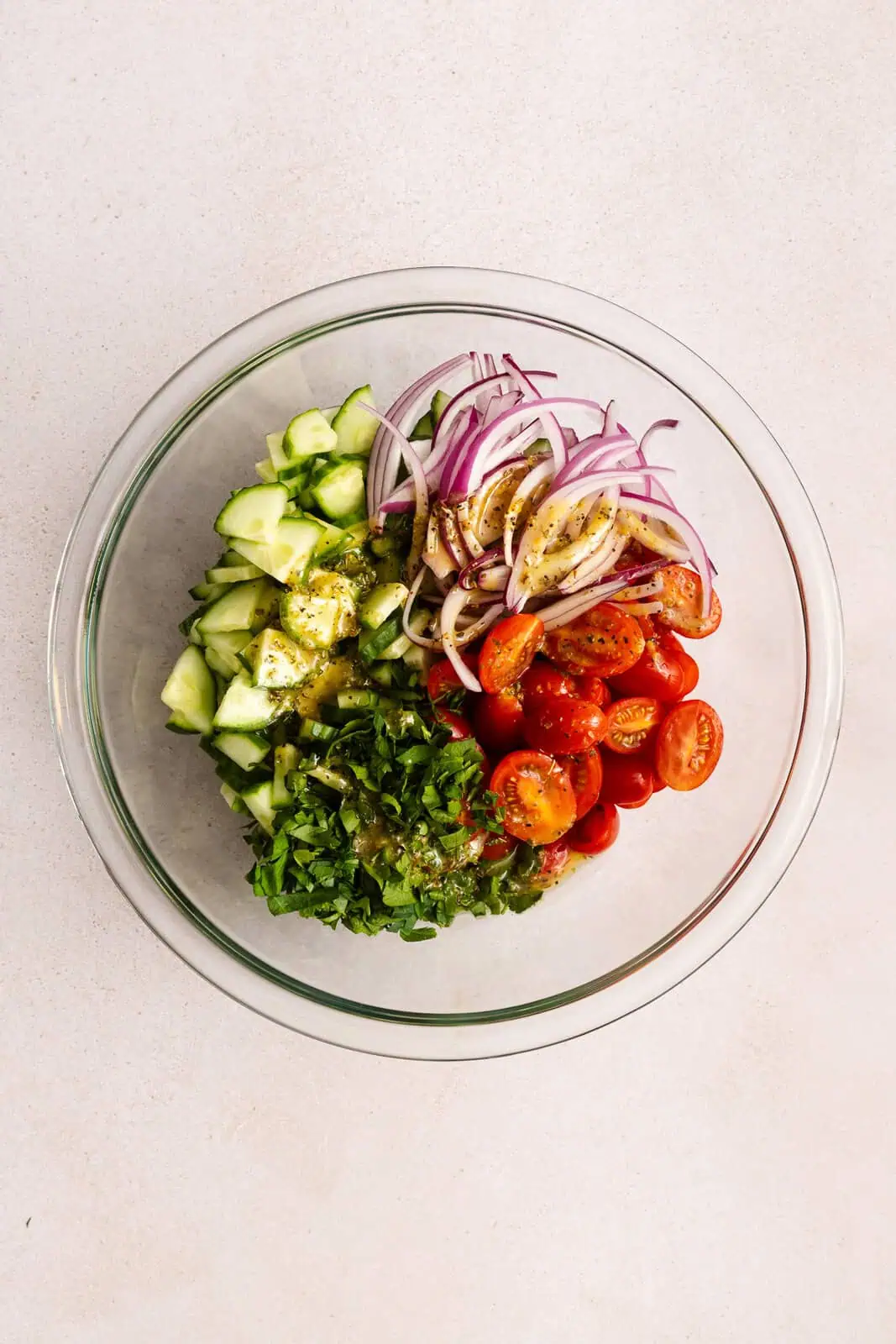 Dressing drizzled over the ingredients for cucumber feta salad in a glass bowl.