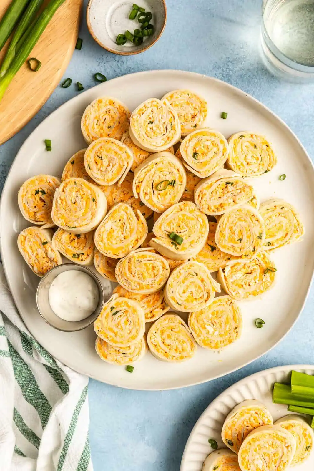 Overhead view of buffalo chicken pinwheels arranged next to a ramekin of ranch dressing on a white platter.