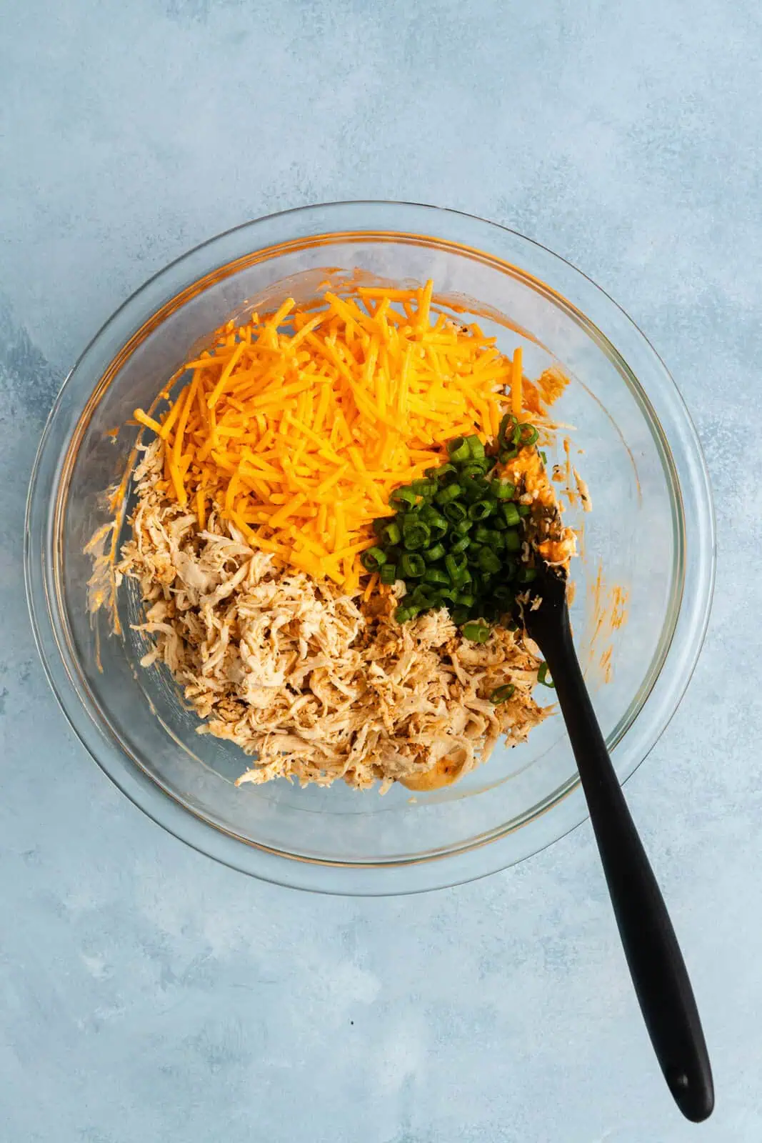 Shredded chicken, shredded cheese, and sliced green onions added to a mixing bowl.