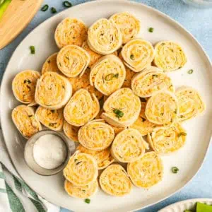 White platter stacked with buffalo chicken pinwheels and a ramekin of ranch dressing.