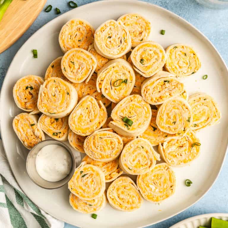 White platter stacked with buffalo chicken pinwheels and a ramekin of ranch dressing.