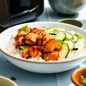 White bowl filled with rice, cucumbers, and air fryer salmon bites.