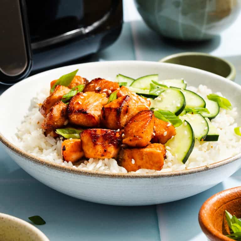 White bowl filled with rice, cucumbers, and air fryer salmon bites.