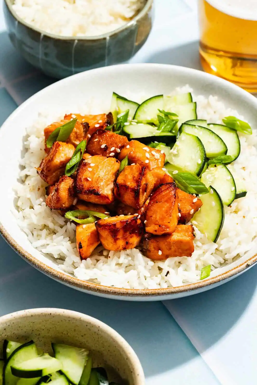 White bowl filled with rice, sliced cucumbers, and air fryer salmon bites.