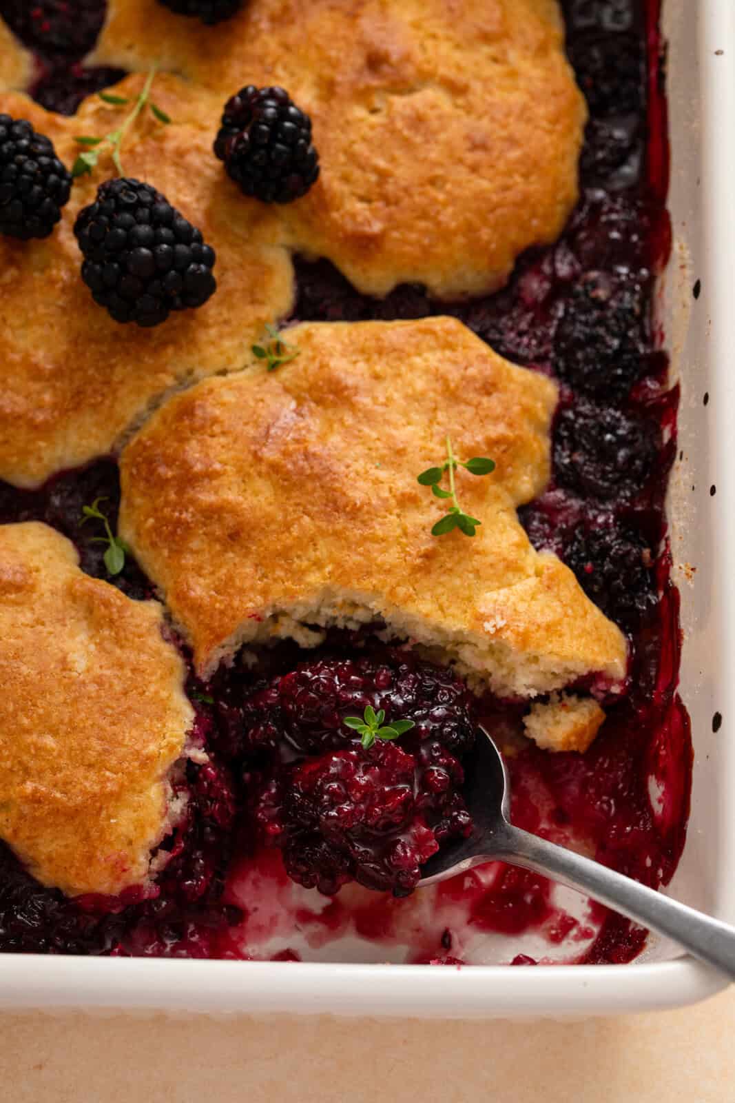 Spoon in the corner of a baking dish filled with biscuit-topped blackberry topping.