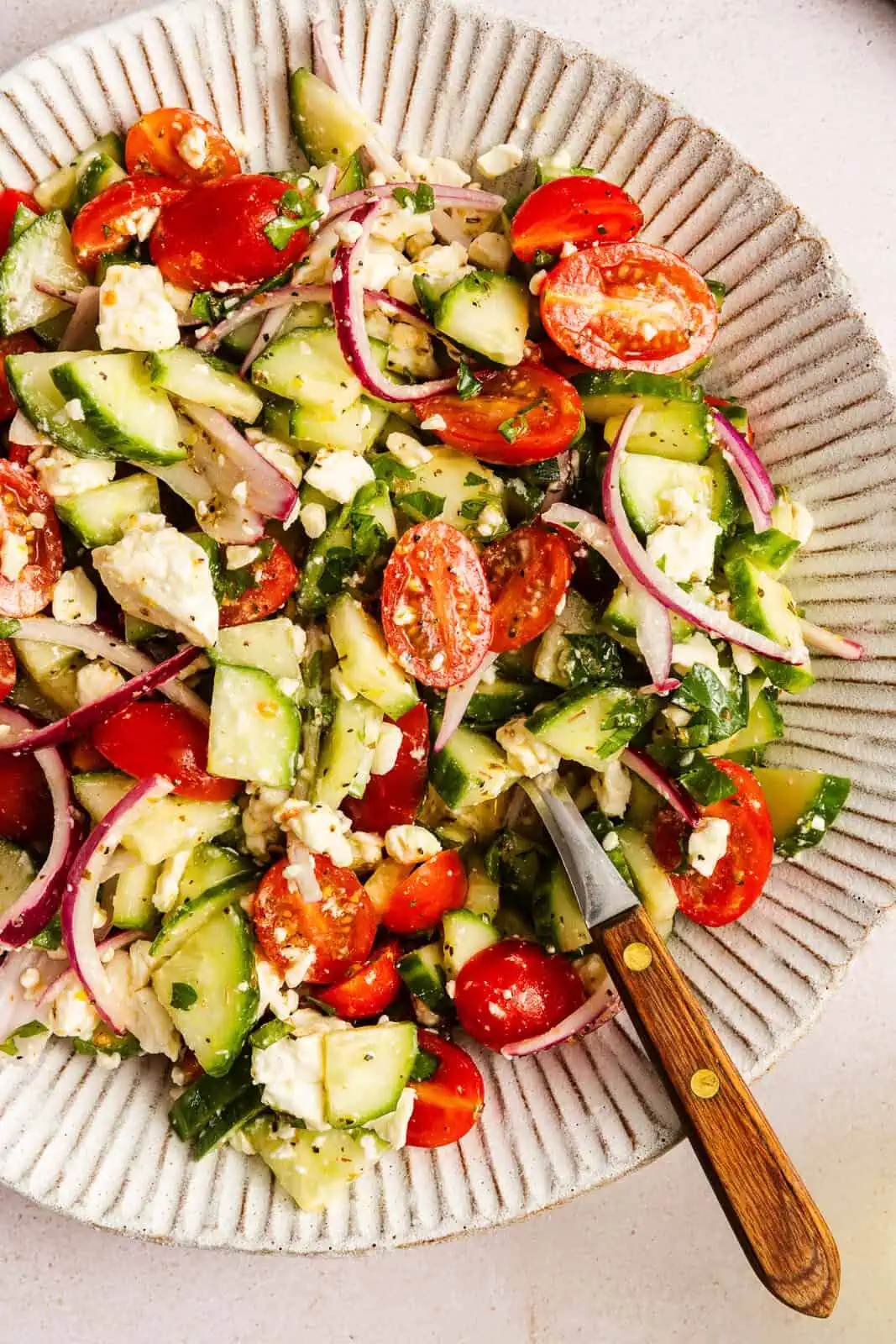 Serving spoon in a large bowl of cucumber feta salad.
