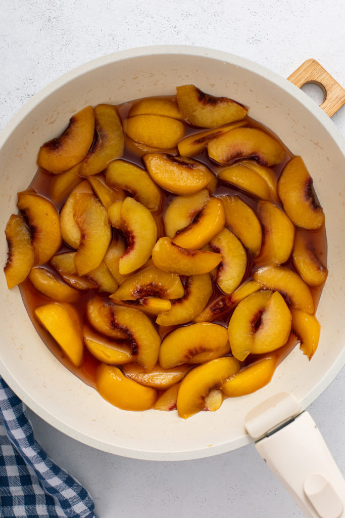 Fresh sliced peaches cooked in syrup in a saucepan.