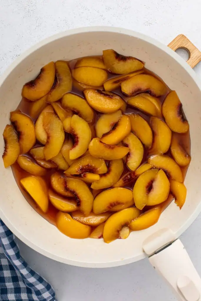 Fresh sliced peaches cooked in syrup in a saucepan.