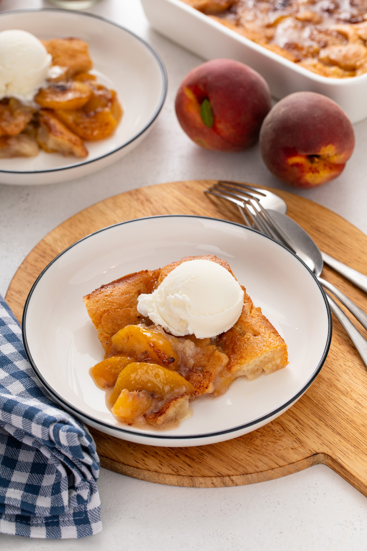 Slice of old-fashioned peach cobbler topped with a scoop of ice cream on a white plate.