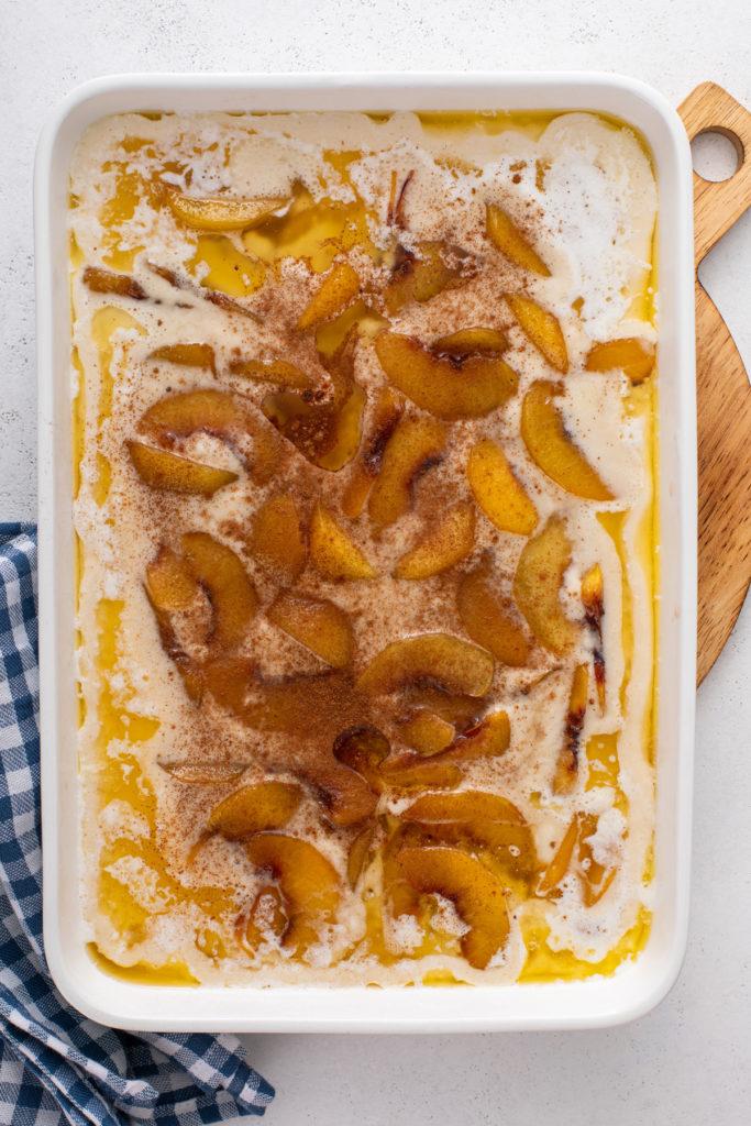 Cooked peaches in syrup layered on top of batter in a baking dish.