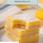 Three lemon bars stacked on a white plate with a bite taken from the corner. Text overlay includes recipe name.