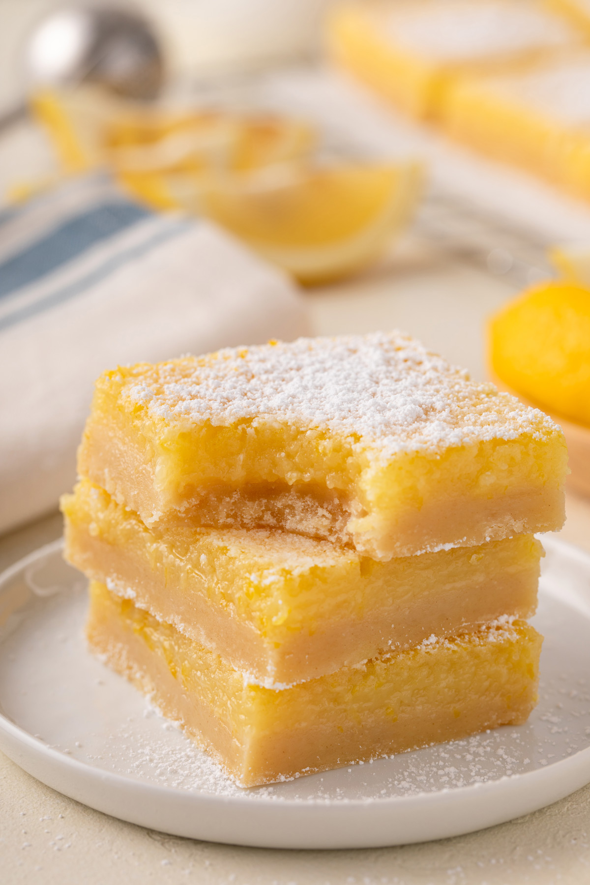 Three lemon bars stacked on a white plate with a bite taken from the corner.