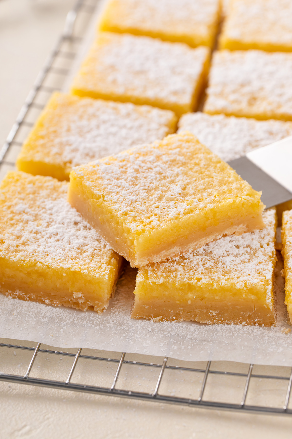 Sliced lemon bar resting on a cake server on top of other sliced lemon bars.