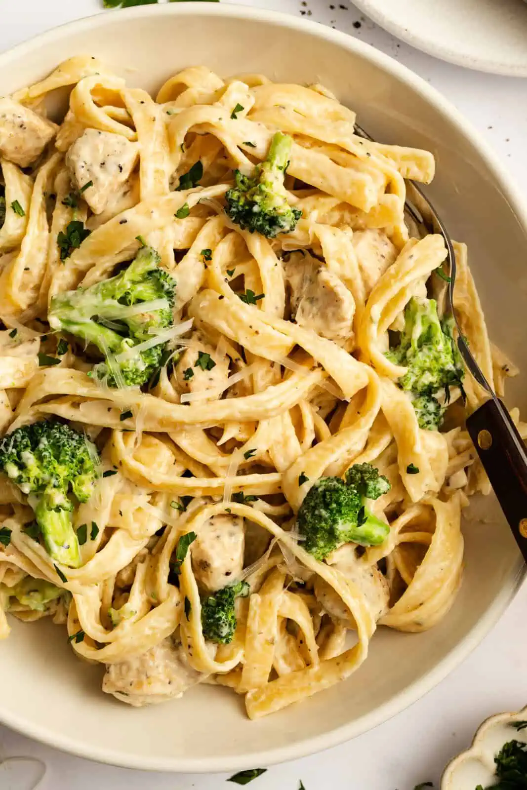 Overhead view of a serving of chicken and broccoli alfredo in a shallow white bowl.
