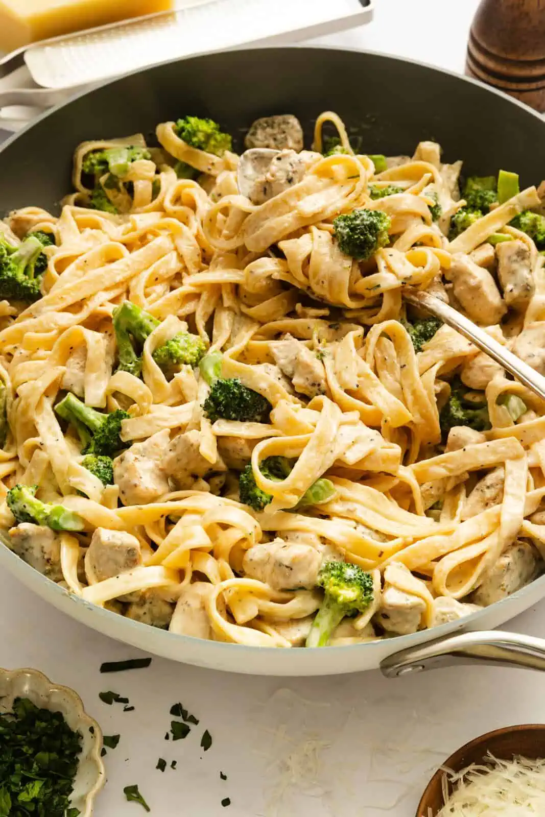 Spoon about to scoop up chicken and broccoli alfredo out of a skillet.