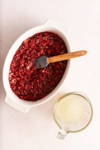 Chopped cranberries mixed with sugar and crushed pineapple in a large dish next to a measuring cup of pineapple juice mixed with water.