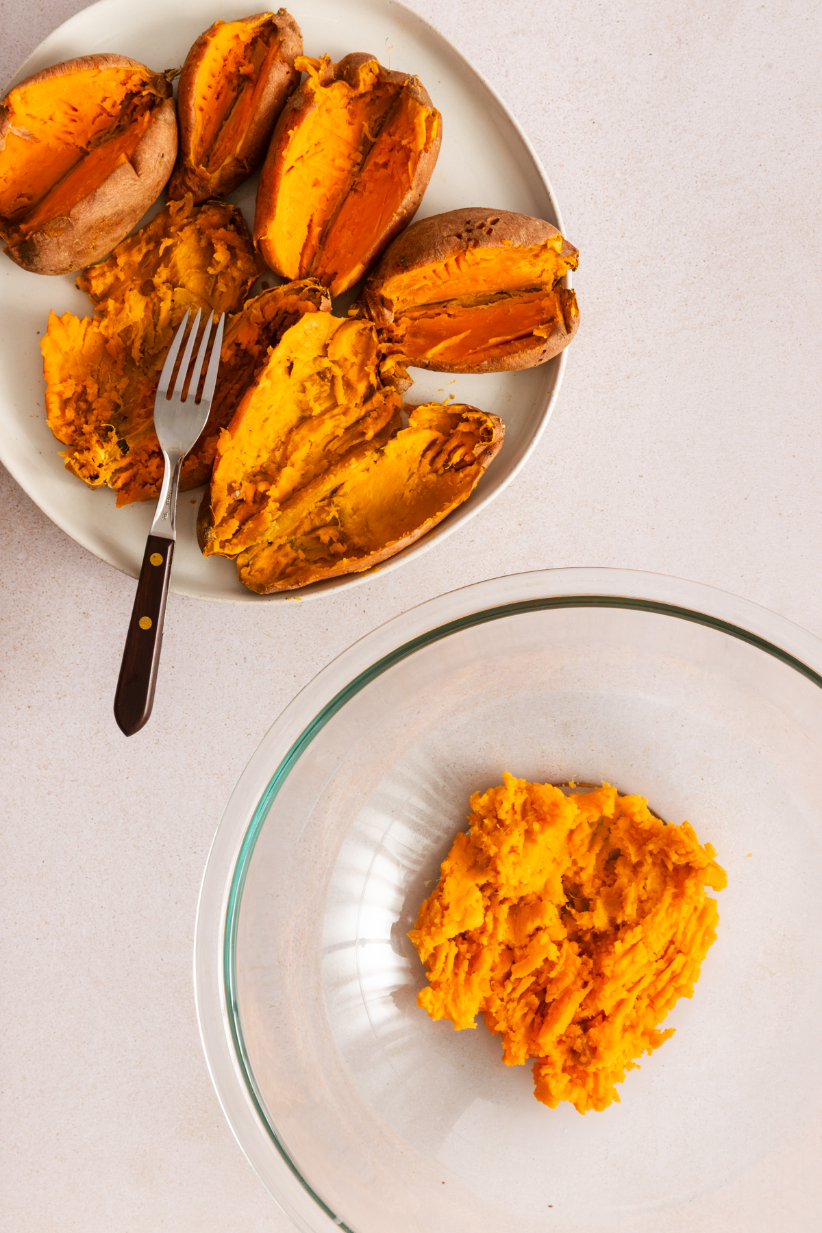 Empty baked sweet potato skins on a plate next to a glass bowl filled with mashed cooked sweet potato.