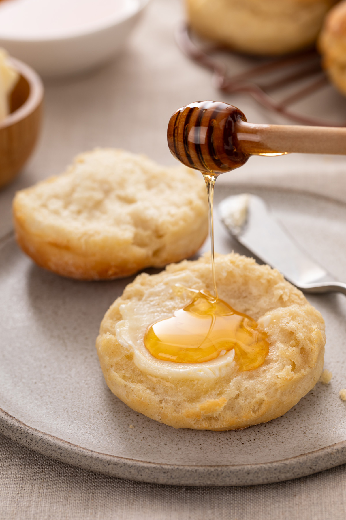 Honey being drizzled onto a halved and buttered angel biscuit on a plate.