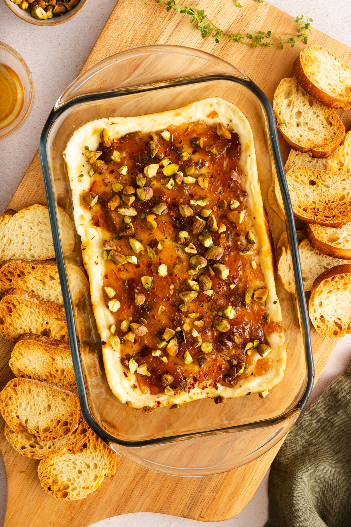 Overhead view of baked goat cheese dip on a wooden board next to toasted baguette slices.