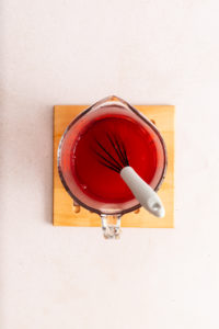 Raspberry gelatin mixed with water and pineapple juice in a measuring cup.