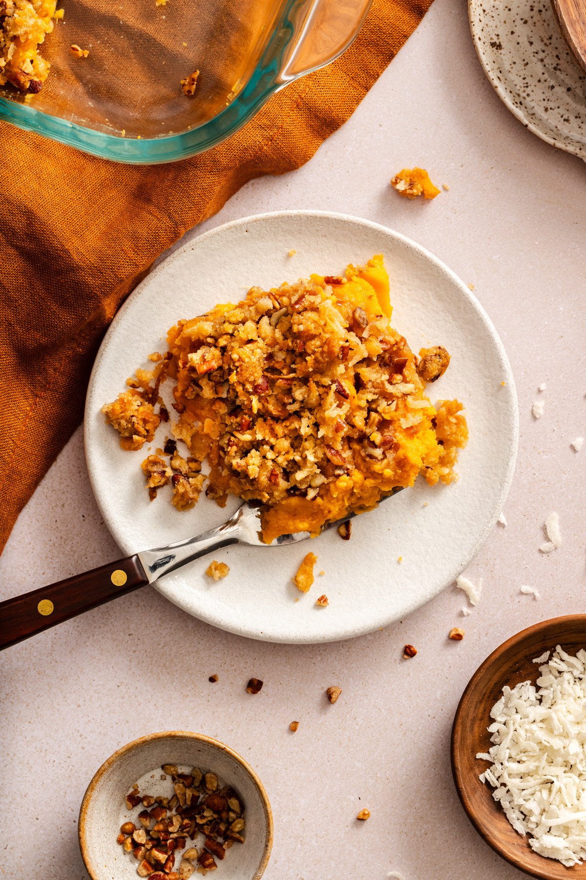 Overhead view of a serving of sweet potato casserole with streusel topping on a white plate next to a rust-orange napkin.