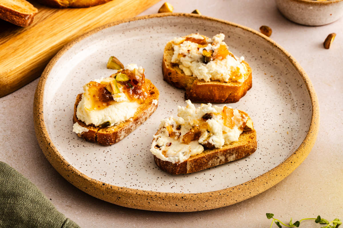 Three crostini topped with baked goat cheese dip on a plate.