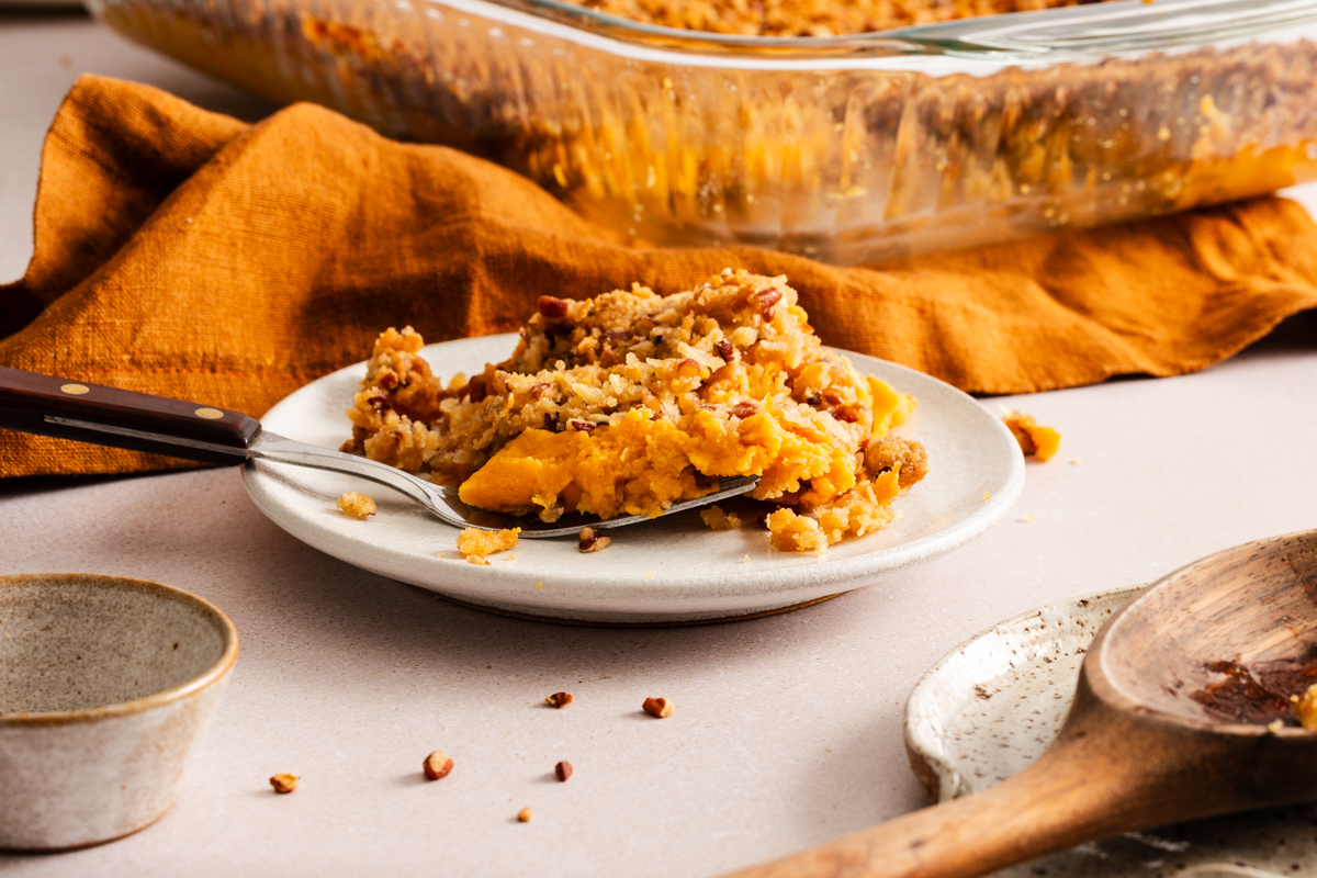 White plate holding a serving of sweet potato casserole with pecan topping.