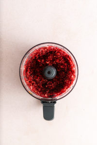 Fresh cranberries chopped with sugar and orange zest in the bowl of a food processor.