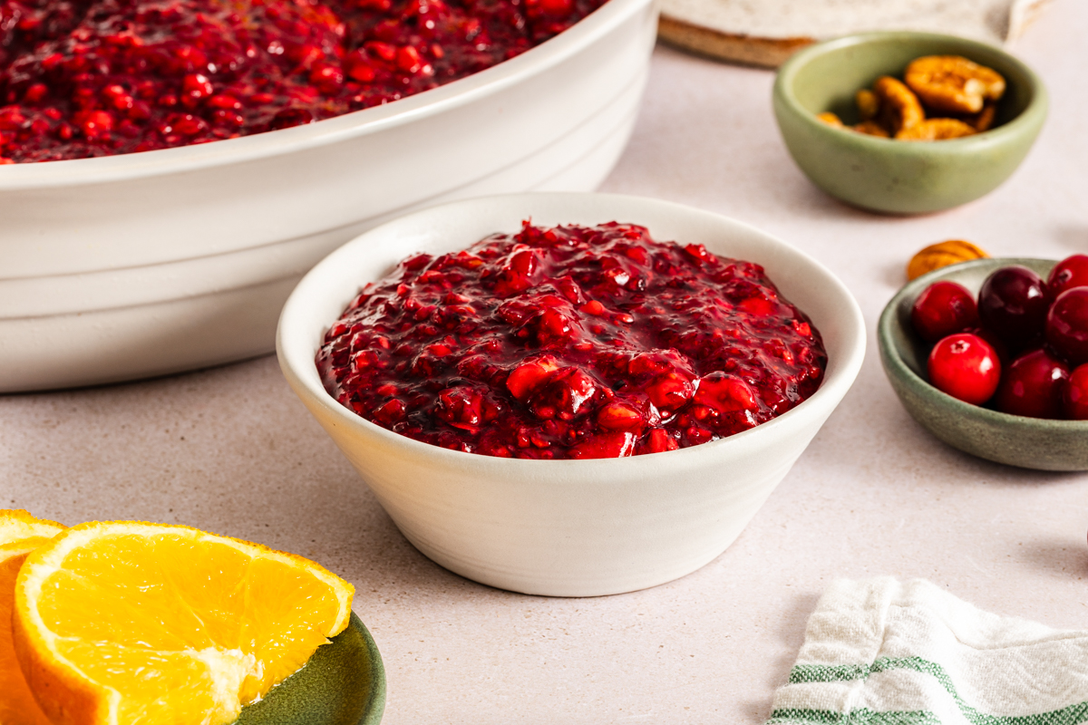Small bowl filled with cranberry jello salad set on a countertop in front of a larger dish of the salad.