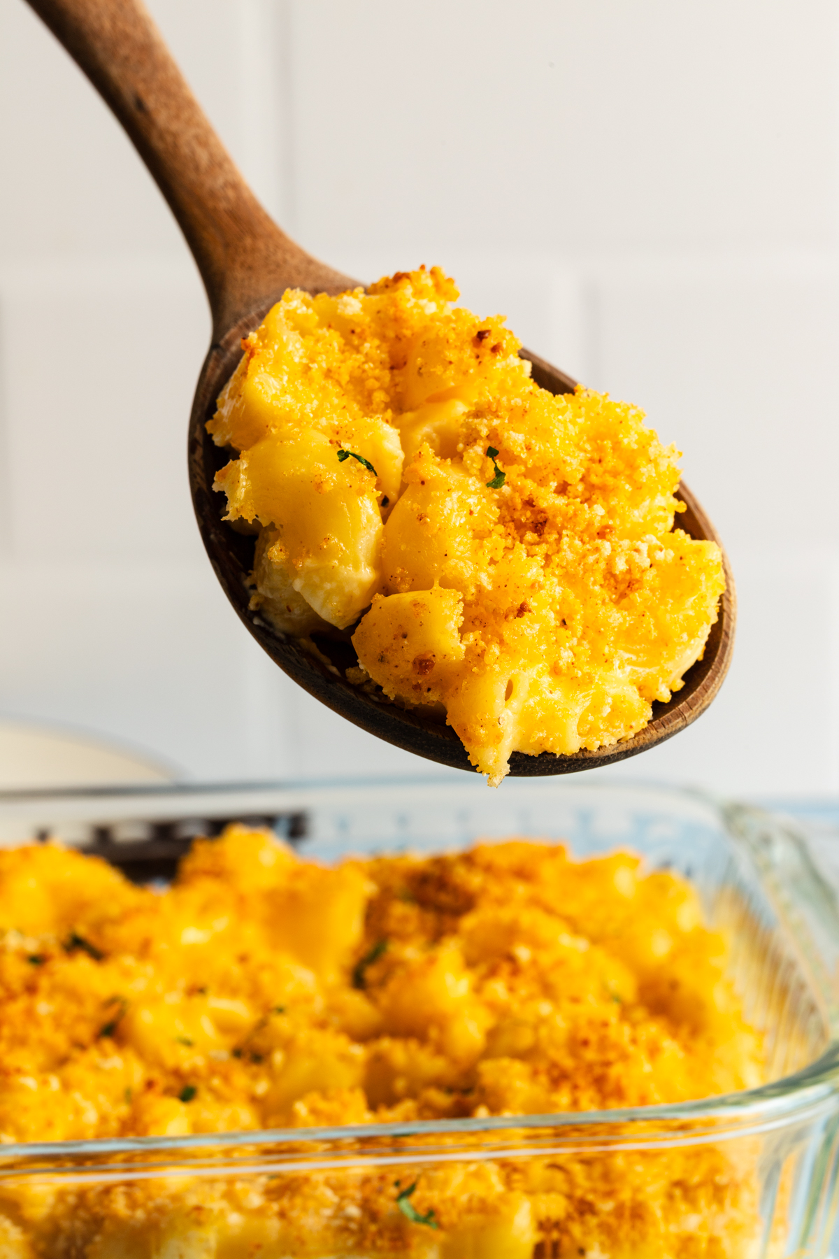 Wooden spoon holding up a serving of smoked gouda mac and cheese above the baking dish.
