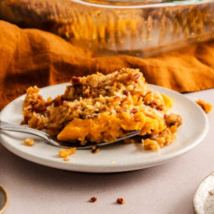 Serving of sweet potato casserole with pecan streusel topping next to a fork on a white plate.