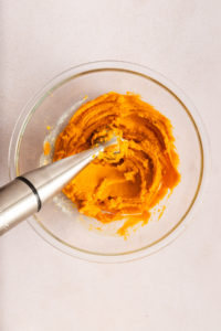 Immersion blender mixing the filling for sweet potato casserole in a glass bowl.