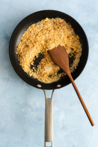 Wooden spoon stirring toasted panko in a black skillet.