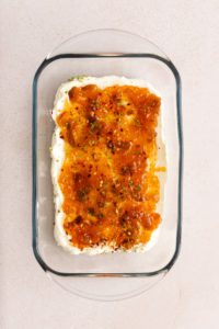 Goat cheese topped with fig jam, red pepper flakes, and thyme spread in a baking dish, ready to go in the oven.
